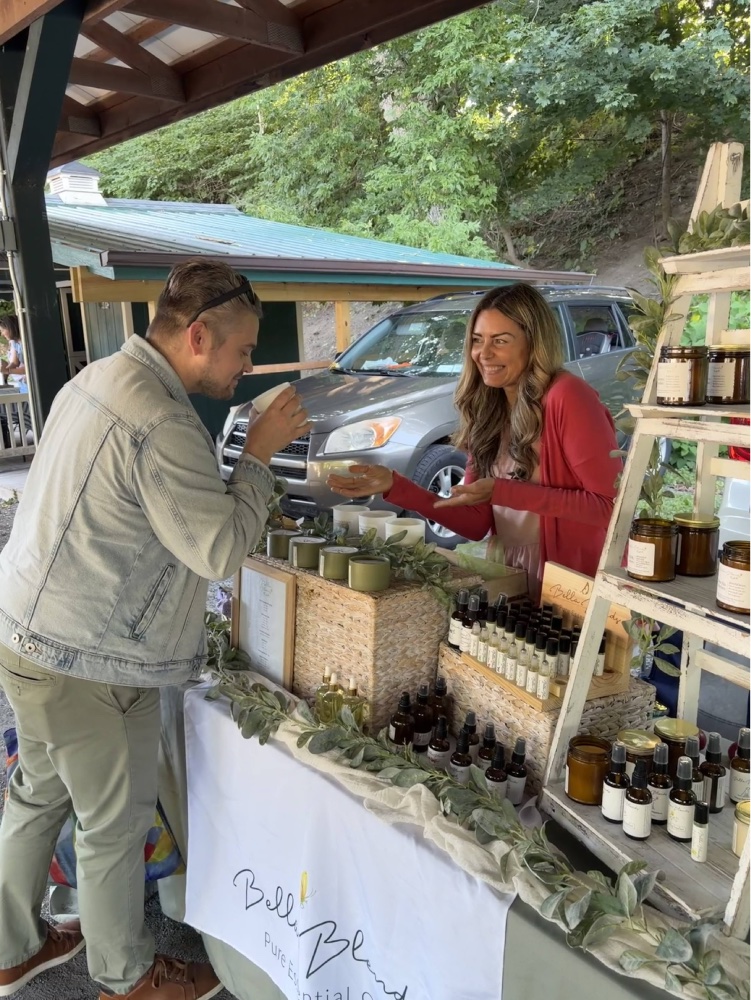 Bella Blends vendor Amy chatting with customer at candle and essential oil booth at Saratoga Farmers Market