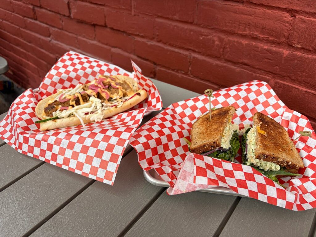 Two sandwiches served in red-and-white checkered paper on outdoor table.