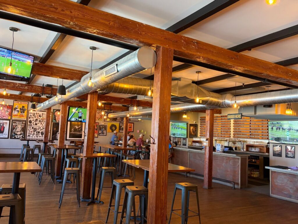 Interior of Whitman Brewing taproom with wooden beams, high top tables and the bar in the background.